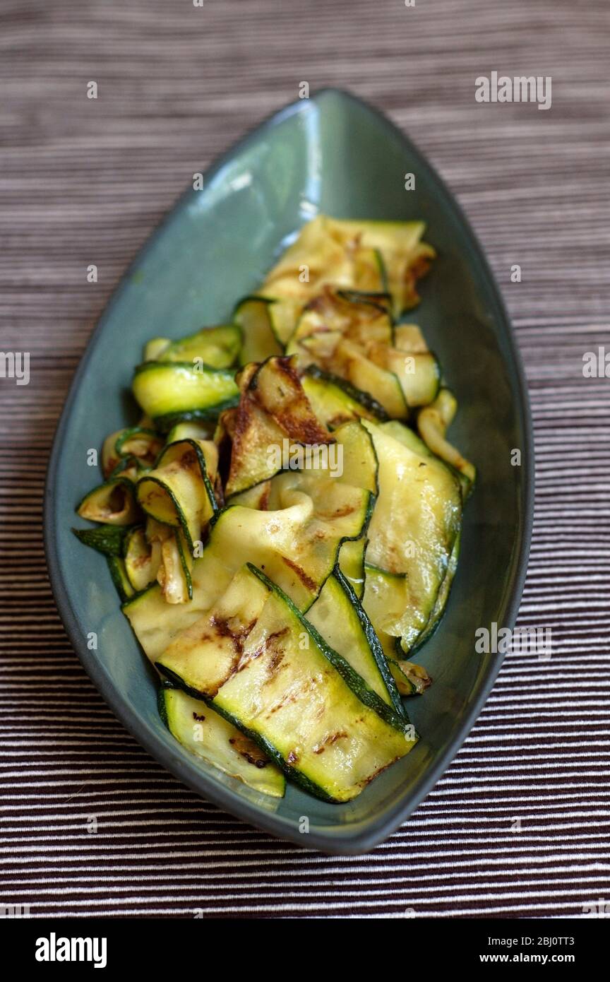 Courgettes finement coupées cuites sur une poêle à griddle, brossées d'huile d'olive et servies sur une plaque verte - Banque D'Images