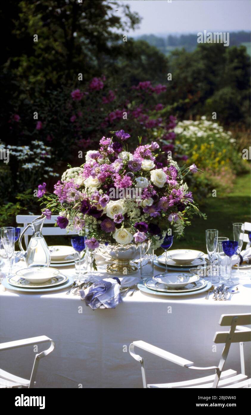 Superbe aménagement de fleurs bleues et blanches au milieu d'une table formelle organisée à l'extérieur dans le jardin d'été - Banque D'Images