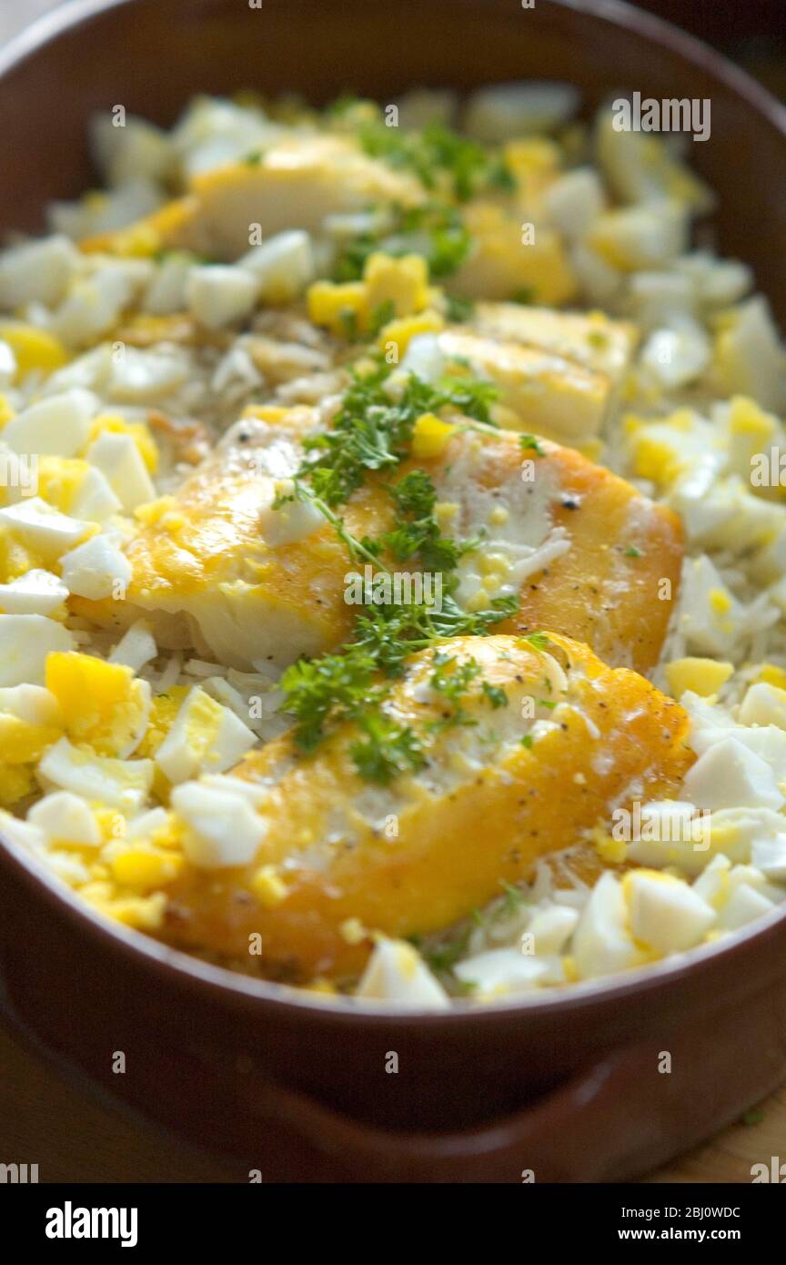 Kedgeree en terre cuite avec des morceaux d'aiglefin fumé assis sur le riz avec des œufs hachés disposés autour - Banque D'Images