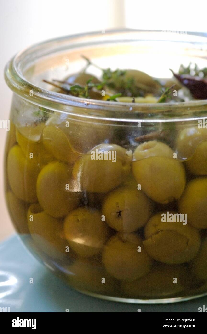 Olives vertes dénoyées dans de l'huile d'olive vierge aromatisées aux branches de thym, de zeste de citron et de piment - Banque D'Images