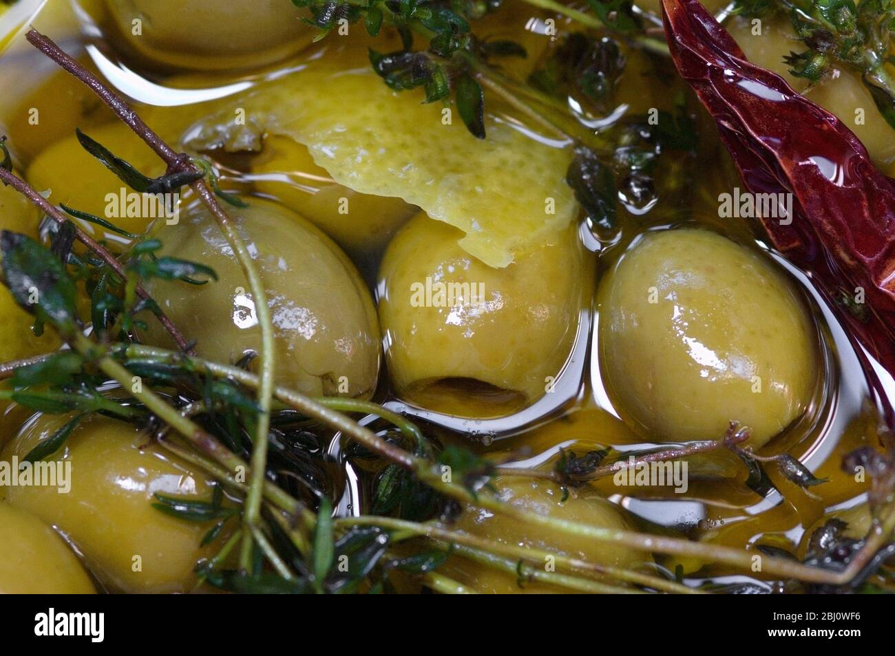 Olives vertes dénoyées dans de l'huile d'olive vierge aromatisées aux branches de thym, de zeste de citron et de piment - Banque D'Images