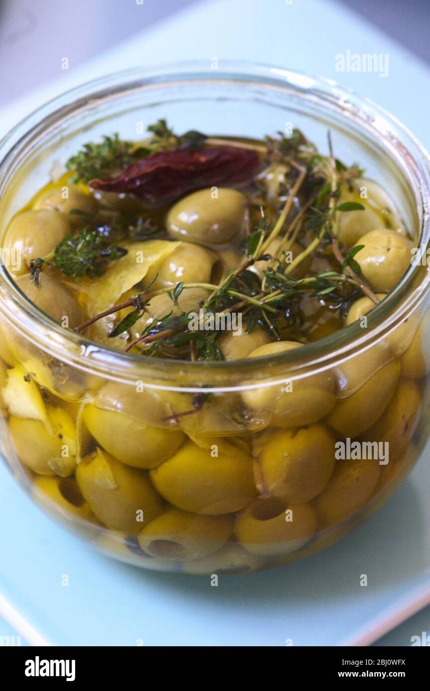 Olives vertes dénoyautées marinées dans de l'huile d'olive vierge aromatisée avec des branches de thym, de zeste de citron et de piment Banque D'Images
