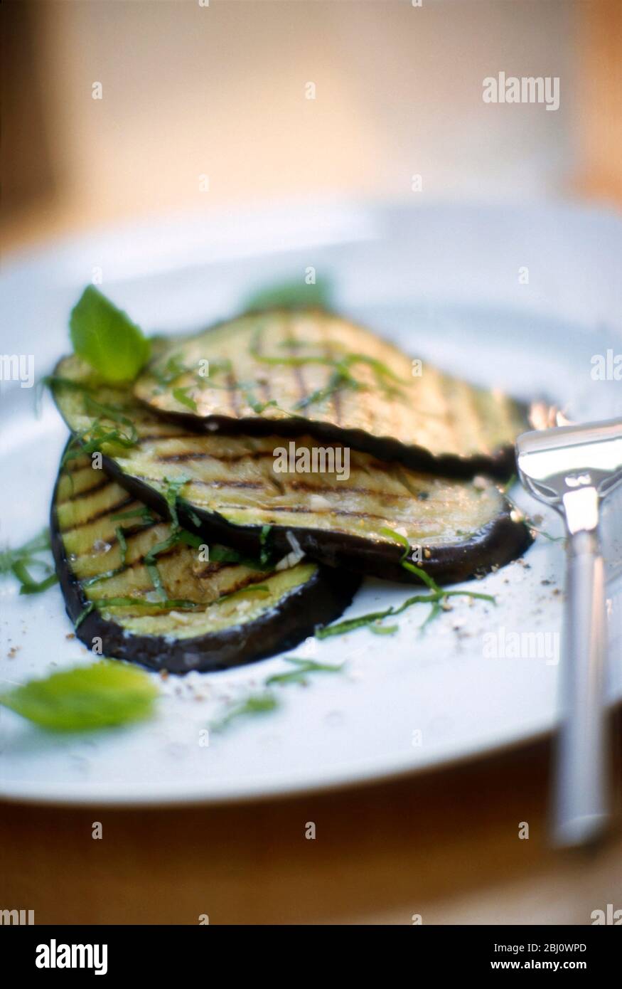 Salade de tranches d'aubergine grillée, avec huile et vinaigre et feuilles de basilic déchiquetées - Banque D'Images