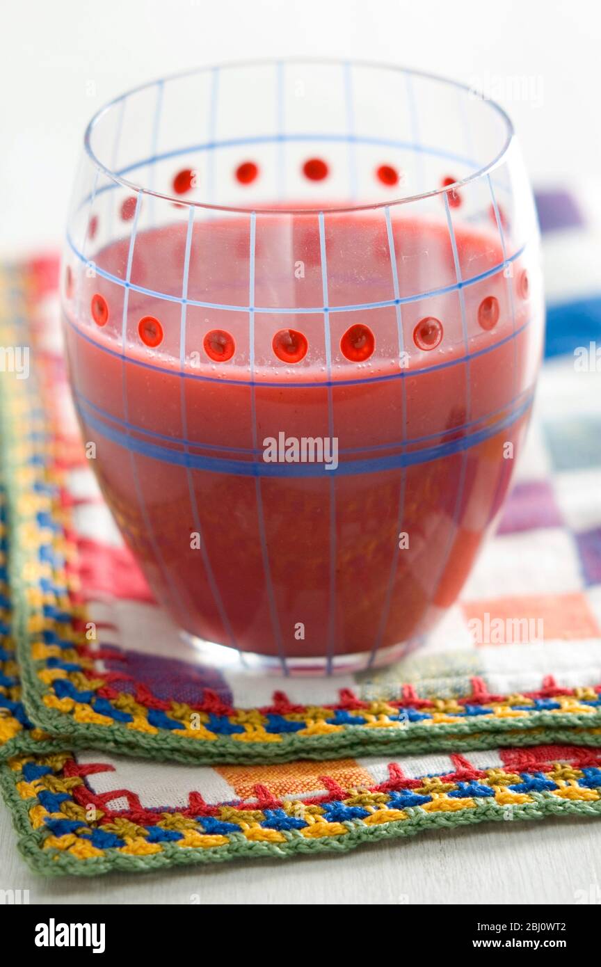 Verre décoratif peint de smoothie rouge à la framboise sur une serviette à carreaux lumineux - Banque D'Images