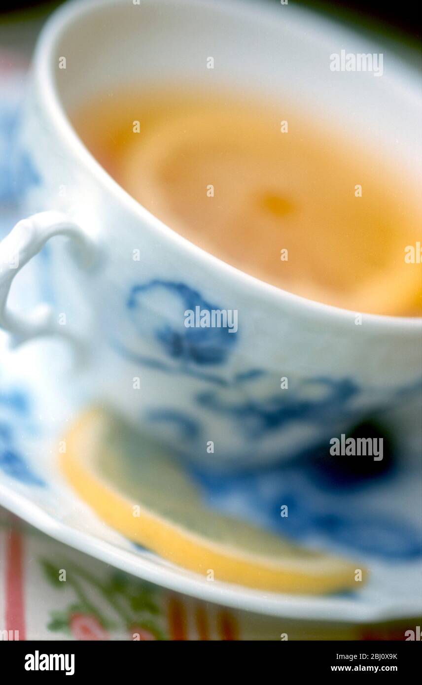 Thé au citron dans une tasse de chine classique, délicate, bleue et blanche sur un tissu rosé - Banque D'Images