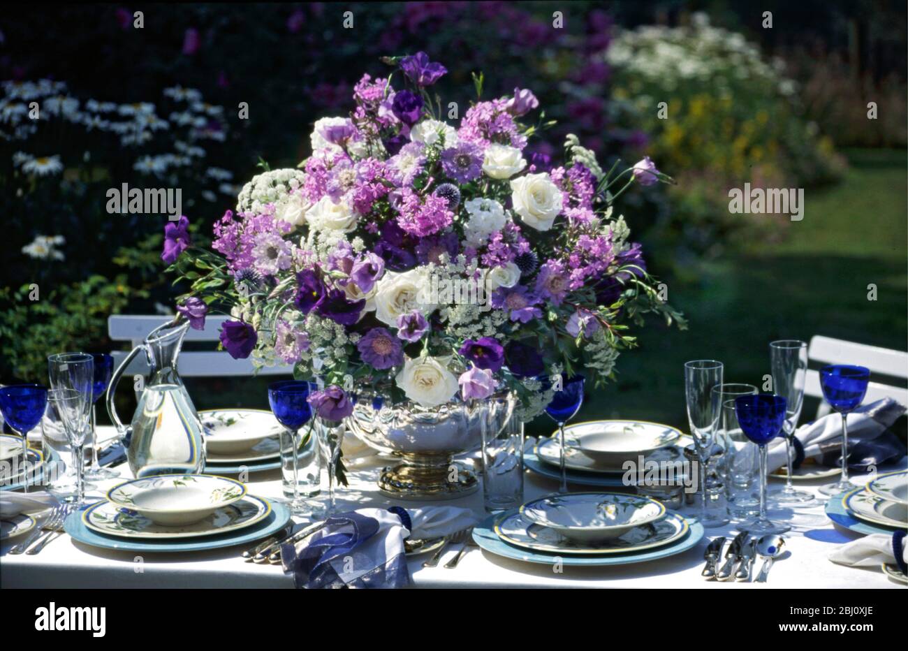 Superbe aménagement de fleurs bleues et blanches au milieu d'une table formelle organisée à l'extérieur dans le jardin d'été - Banque D'Images