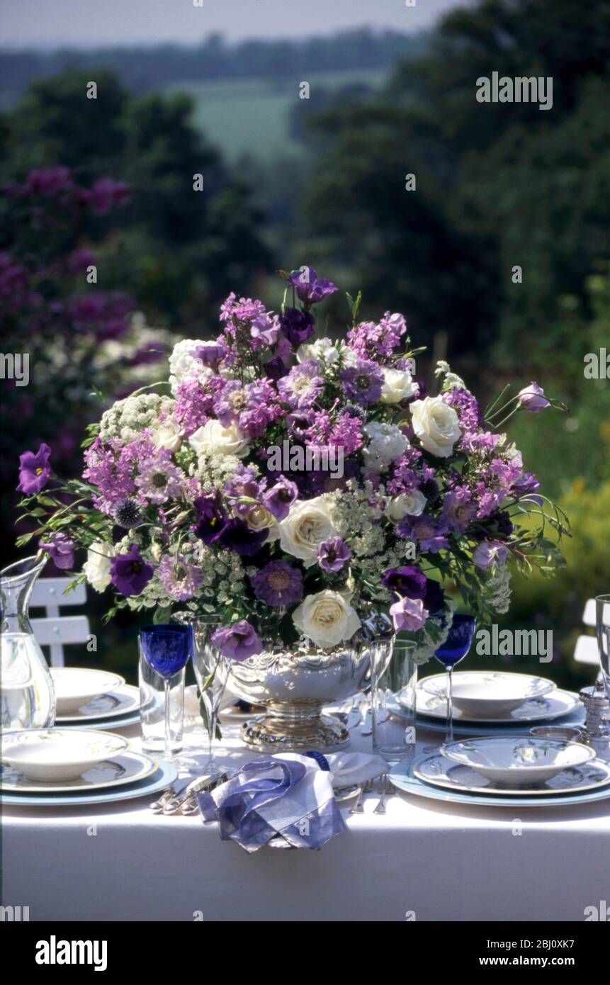 Superbe aménagement de fleurs bleues et blanches au milieu d'une table formelle organisée à l'extérieur dans le jardin d'été - Banque D'Images