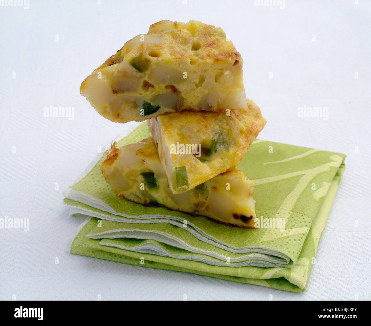 Morceaux de tortilla aux œufs et aux légumes empilés sur une serviette en papier vert plié - Banque D'Images