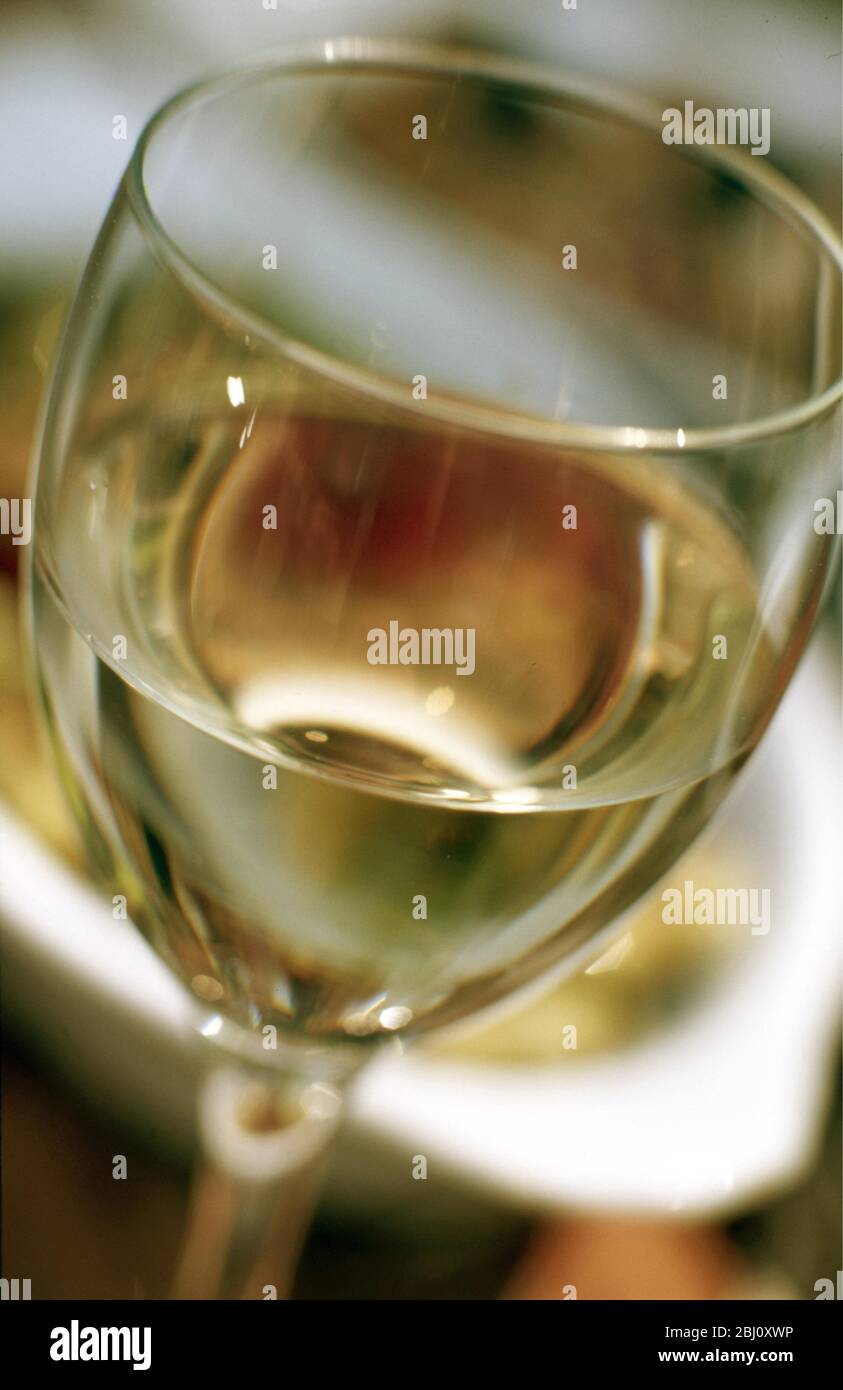 Gros plan sur un verre de vin blanc avec des plats de la nourriture derrière - - Banque D'Images