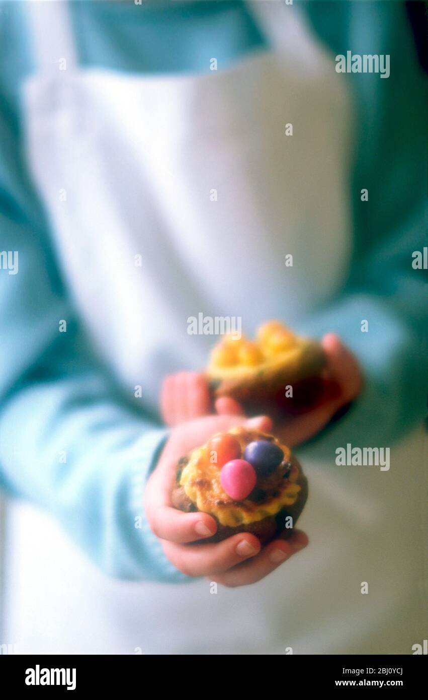 Petits gâteaux avec mini œufs de pâques dans les mains de l'enfant - Banque D'Images