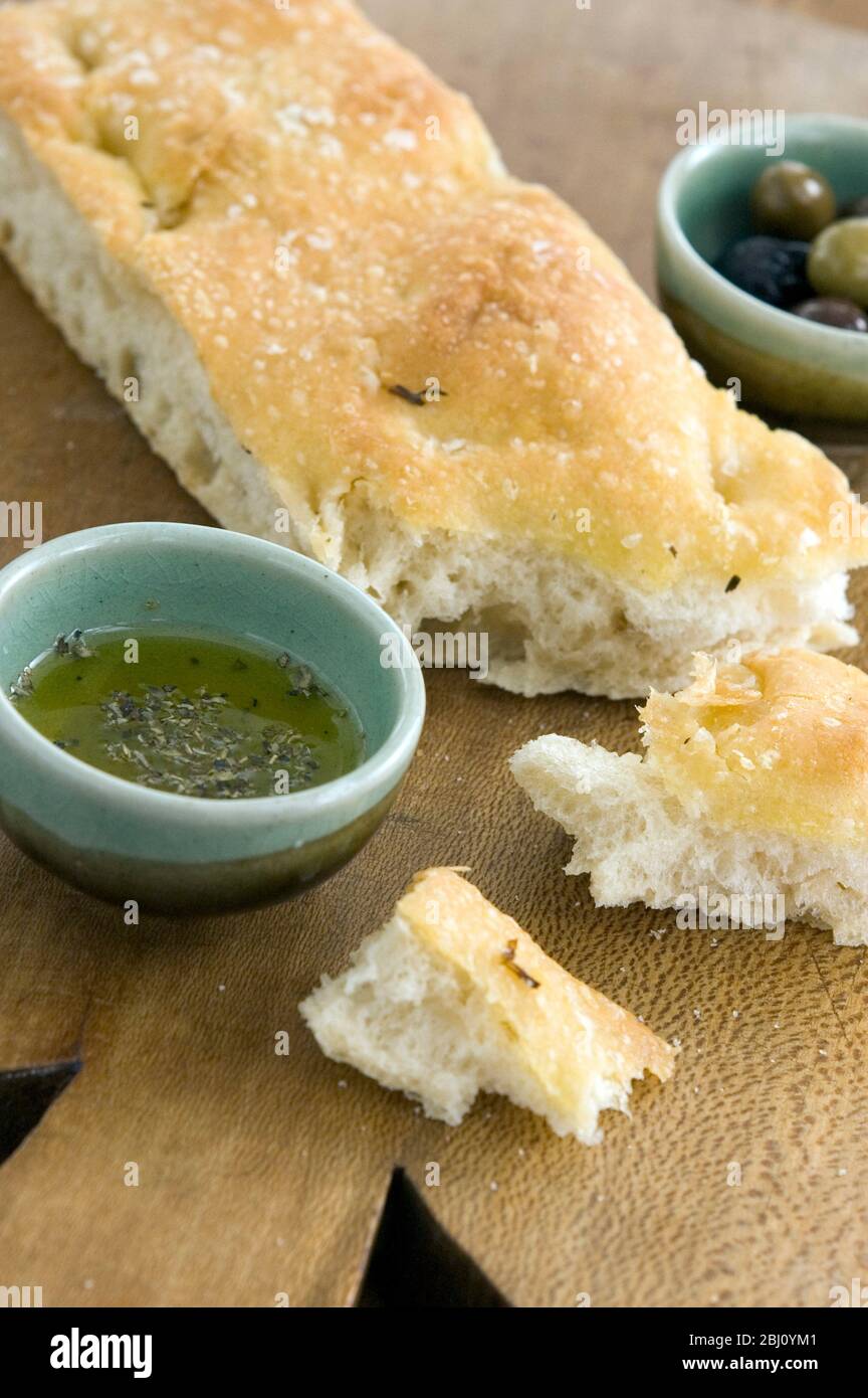 Huile d'olive et pain de focaccia au romarin sur carton de bois avec petits bols d'huile d'olive herbed et des olives entières - Banque D'Images