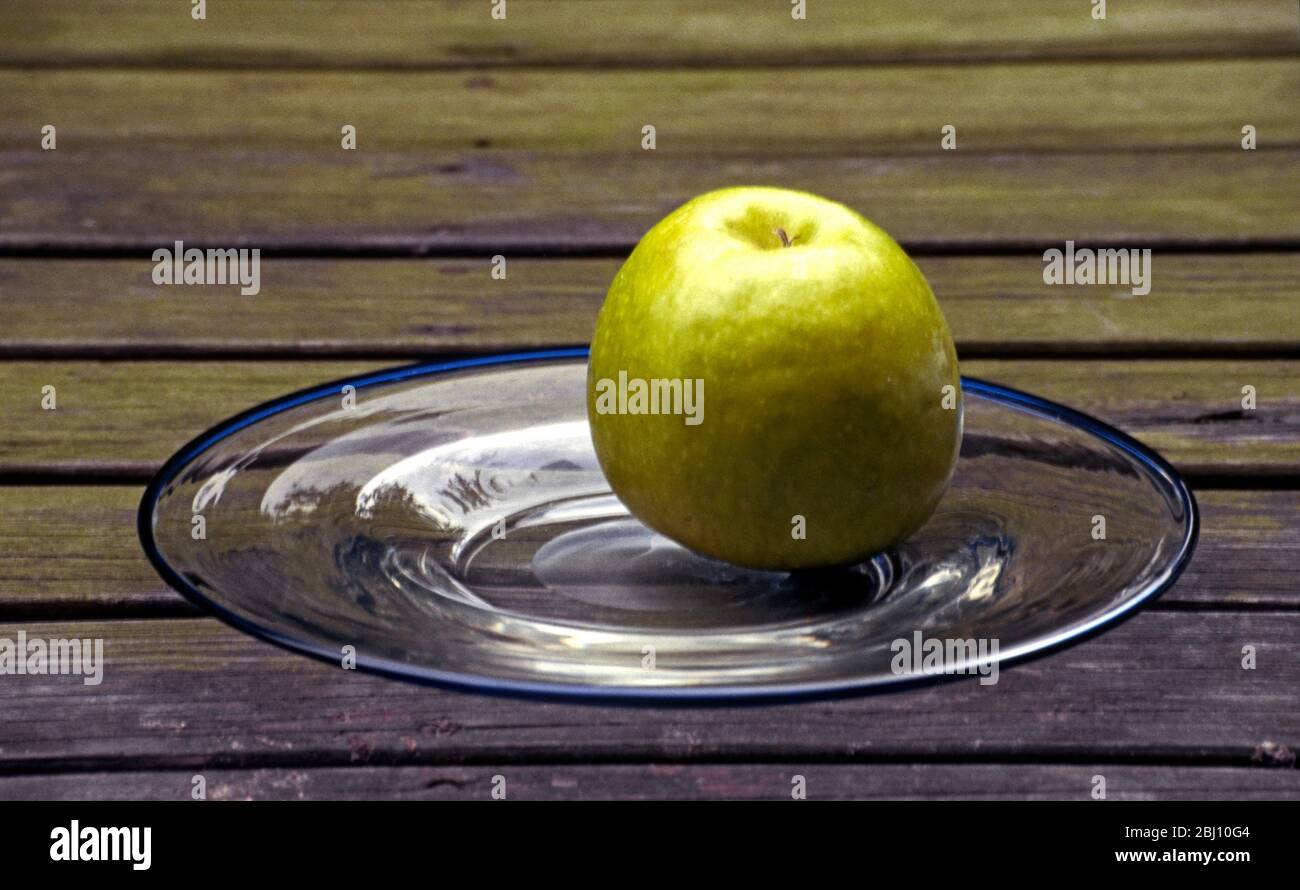 Pomme verte sur plaque de verre transparente sur l'ancienne table en bois - Banque D'Images