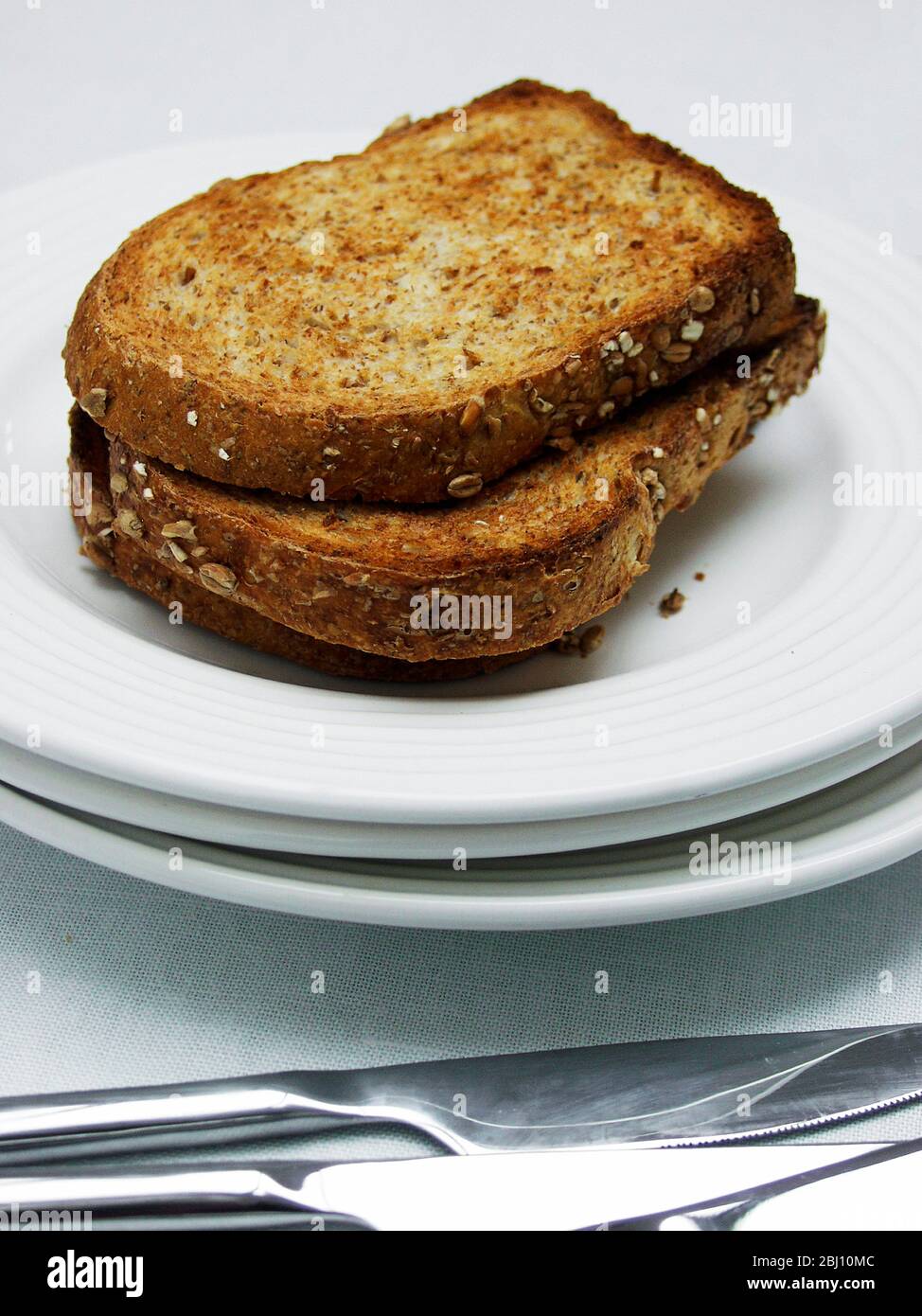 Trois tranches de toast complet marron sur une pile de plaques blanches avec couverts - Banque D'Images
