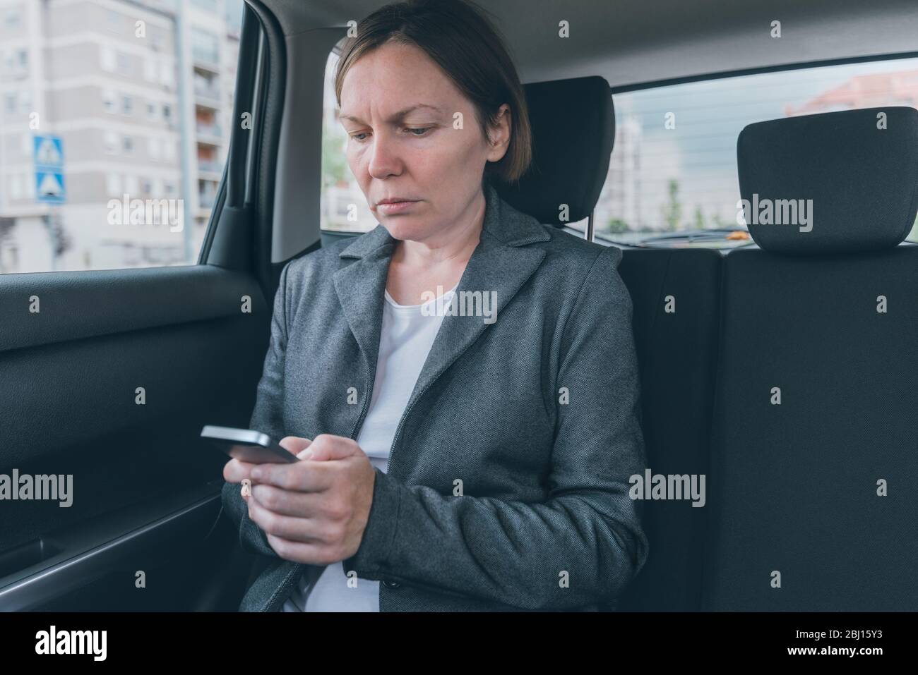 Businesswoman text messaging on mobile phone in car assis à la banquette arrière, selective focus Banque D'Images