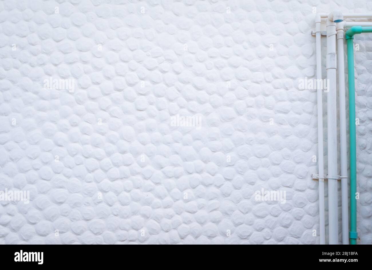 Décoration d'arrière-plan en béton blanc avec petit point rond convexe. Installation d'un tuyau d'alimentation en eau à l'extérieur du bâtiment. Mur de ciment blanc Banque D'Images