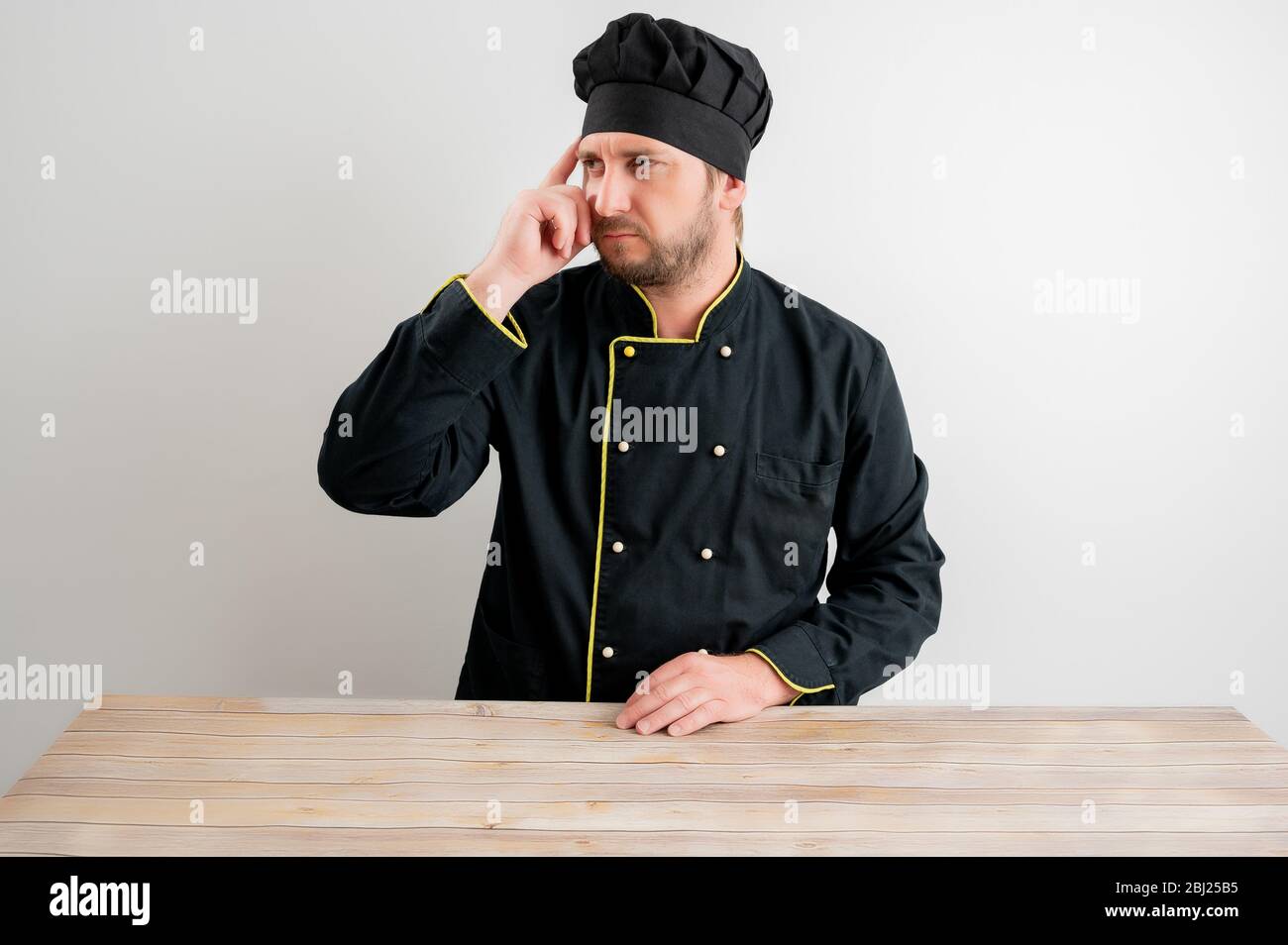 Jeune chef mâle en uniforme noir se demandant poser sur un fond blanc isolé. Banque D'Images