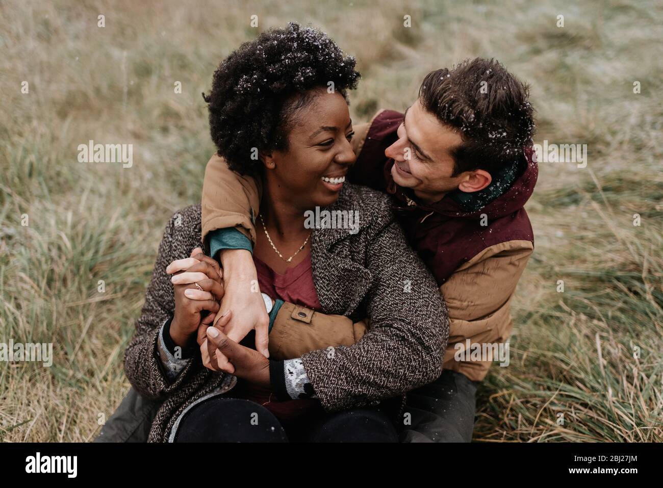 Une femme noire et un homme blanc se embrassant et souriant assis