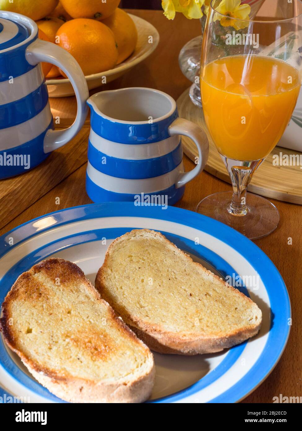 Table de cuisine en bois posée avec service de Cornishware avec pain grillé d'avoine beurré et un verre de jus d'orange frais Banque D'Images