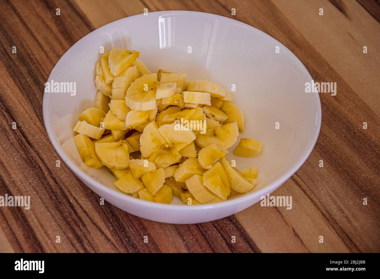 Bol blanc avec petites pièces de banane jaune sur une table en bois Banque D'Images