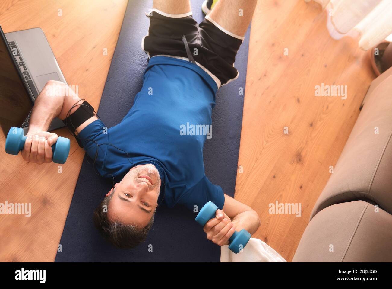 Homme faisant du sport avec des haltères allongé sur le tapis dans le salon à la maison écoutant de la musique avec casque et téléphone. Vue de dessus Banque D'Images