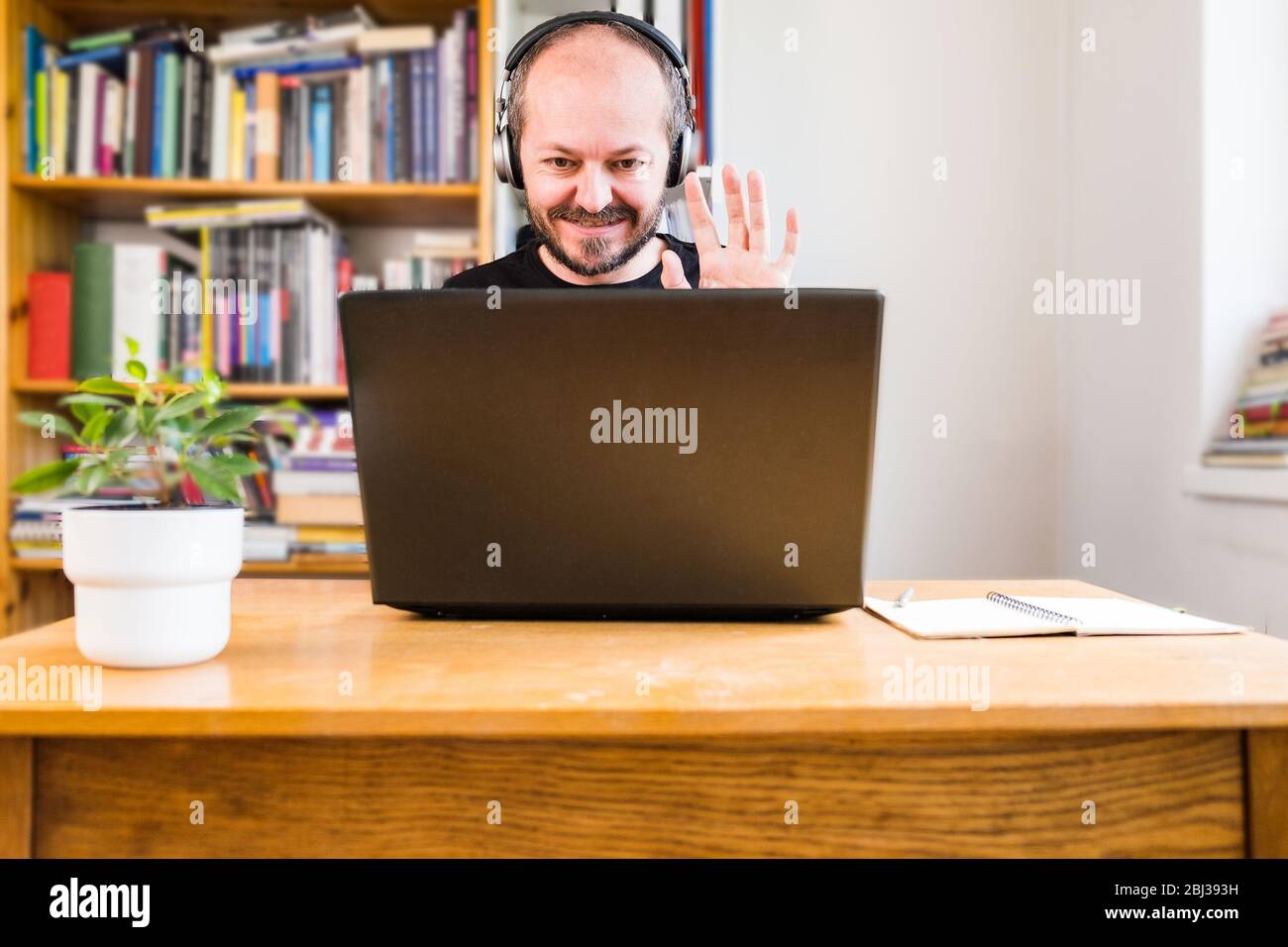 Homme travaillant à domicile, par téléconférence. Homme barbu travaillant en ligne de la maison sur ordinateur portable derrière un bureau vintage avec fleur dans vase, avec Banque D'Images