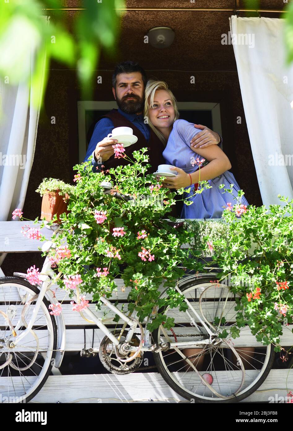 Déjeuner et concept romantique. Couple amoureux tient des tasses de café à l'extérieur. Fille avec cheveux blond et barbu gars sur fond de café. Femme et homme avec des visages calmes ont une date sur la terrasse avec vélo Banque D'Images