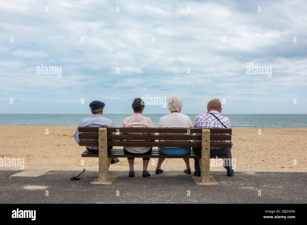 Vue arrière de quatre personnes âgées anonymes, de vieux couples, de vieux hommes et de femmes assis sur un banc à la plage Banque D'Images