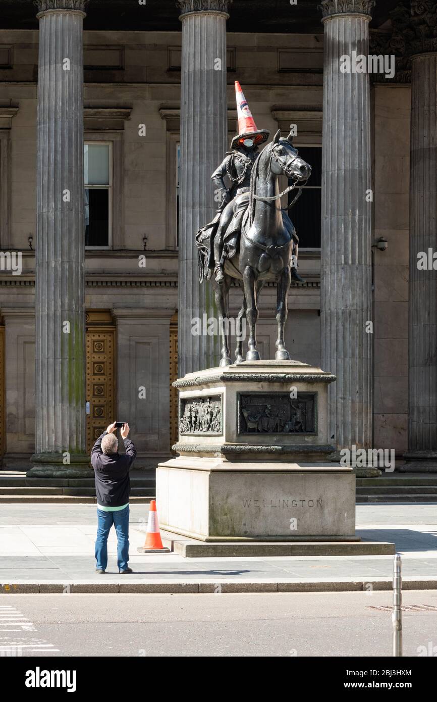 Glasgow, Écosse, Royaume-Uni. 28 avril 2020. Glasgow pendant le verrouillage de Coronavirus. Un homme prend une photo du déjeuner de l'emblématique statue du duc de Wellington portant un masque de visage crédit: Kay Roxby/Alay Live News Banque D'Images