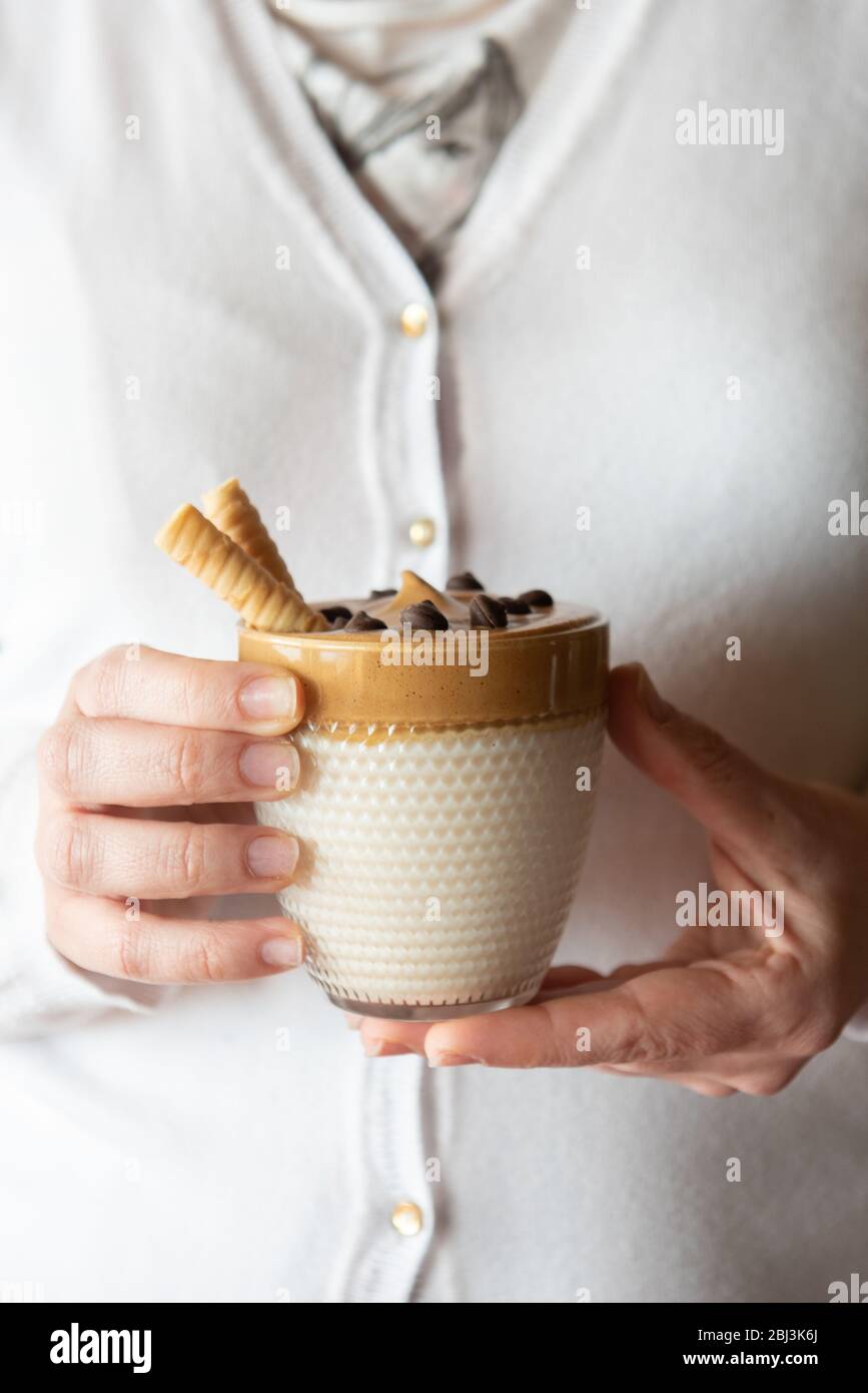 Les mains féminines tiennent le café de dalgon fait maison dans un verre avec du lait sur un support en bois. Café crémeux et tendance à la crème fouettée. Banque D'Images
