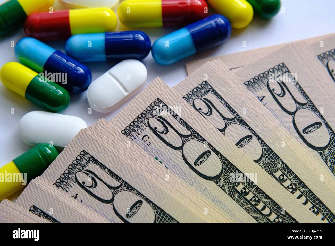 Pile de pilules de différentes couleurs telles que le bleu, le jaune, le rouge et le blanc placé à côté de 50 dollars de factures. Illustration du coût des factures médicales, santé Banque D'Images