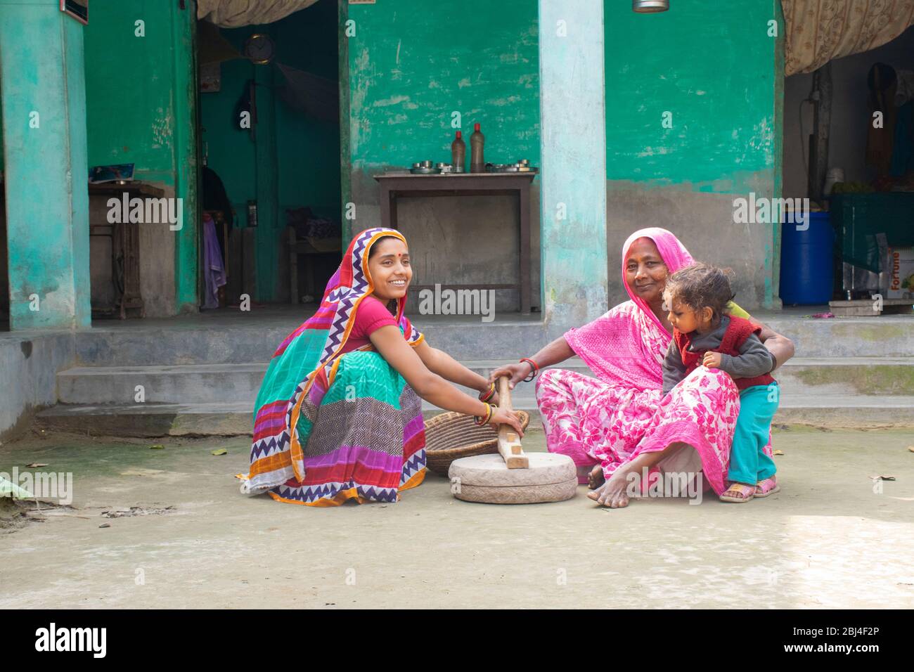 Femme indienne tenant un enfant et meuler de la farine dans un village Banque D'Images