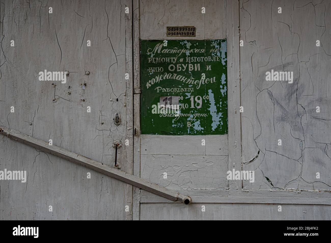 Panneau vert obsolète avec lettrage cyrillique à l'ancienne sur fond gris de mur blanc rayé. Extérieur du bâtiment rétro. Banque D'Images