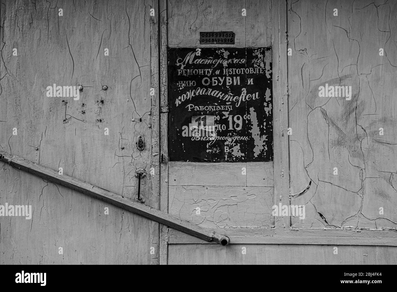 Photo en noir et blanc d'un panneau de signalisation obsolète avec des lettres en caractères cyrilliques à l'ancienne sur fond gris de mur blanc rayé. Détails de l'ancien buildin Banque D'Images