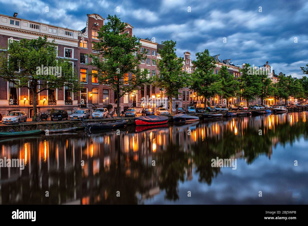 Amsterdam, pays-Bas. Les maisons élégantes se reflètent sur le canal sur la rivière Amstel, à la première lumière de la soirée avec des bateaux ancrés. Banque D'Images