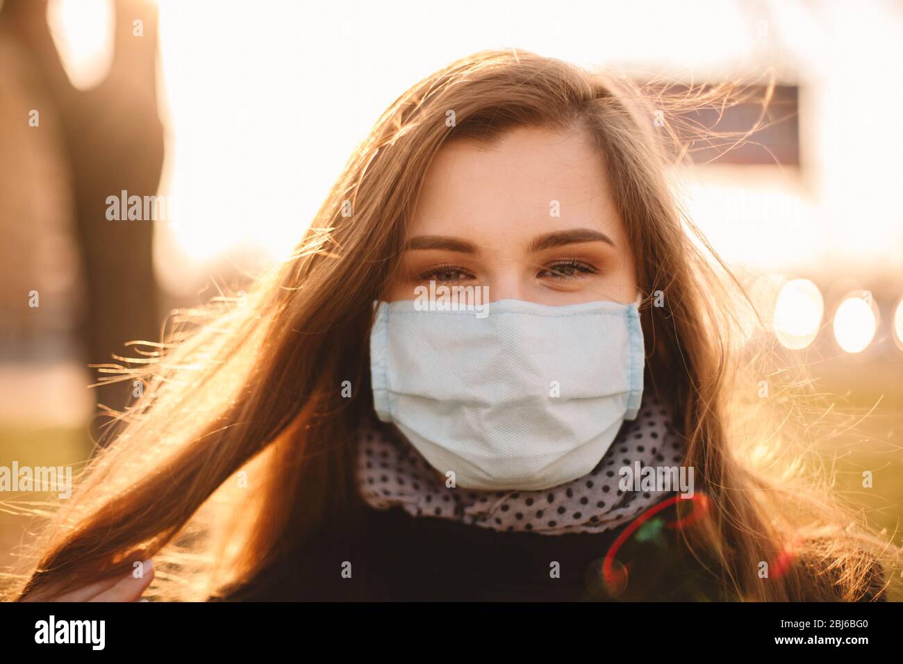 Portrait de heureuse jeune femme portant un masque médical protecteur face debout en ville au coucher du soleil Banque D'Images