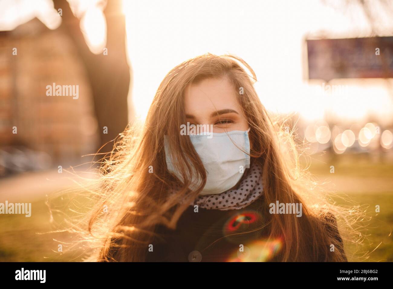 Portrait de heureuse jeune femme portant un masque médical protecteur face debout en ville au coucher du soleil Banque D'Images
