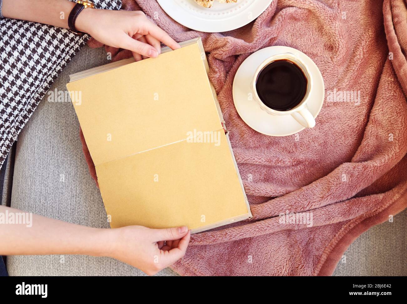 Mains féminines avec livre ouvert, plat, fruits et café sur le canapé. Vue de dessus Banque D'Images