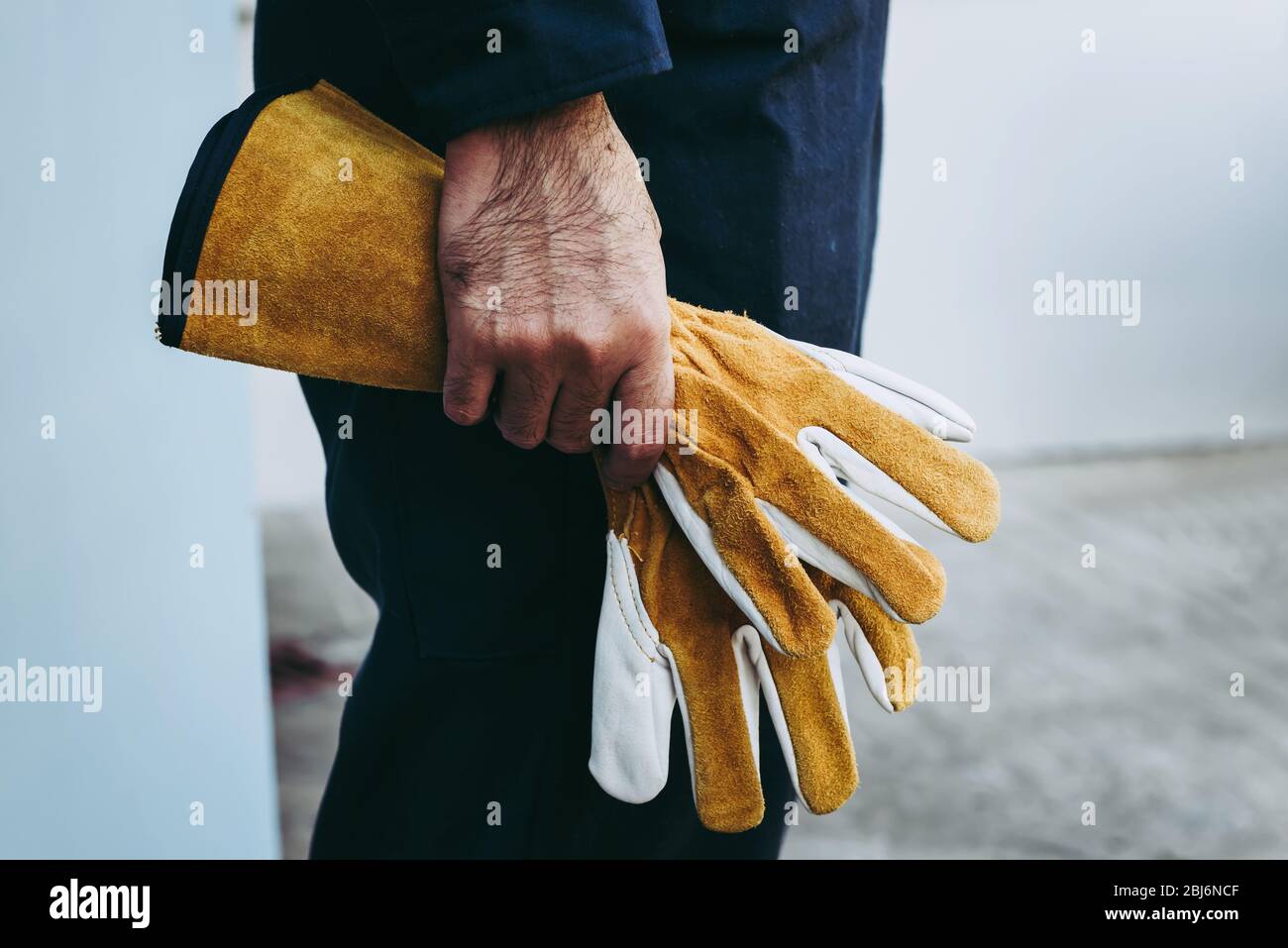 La main du technicien mécanicien tient des gants en cuir en se tenant devant de l'atelier d'entretien, préparation du technicien de maintenance technique f Banque D'Images