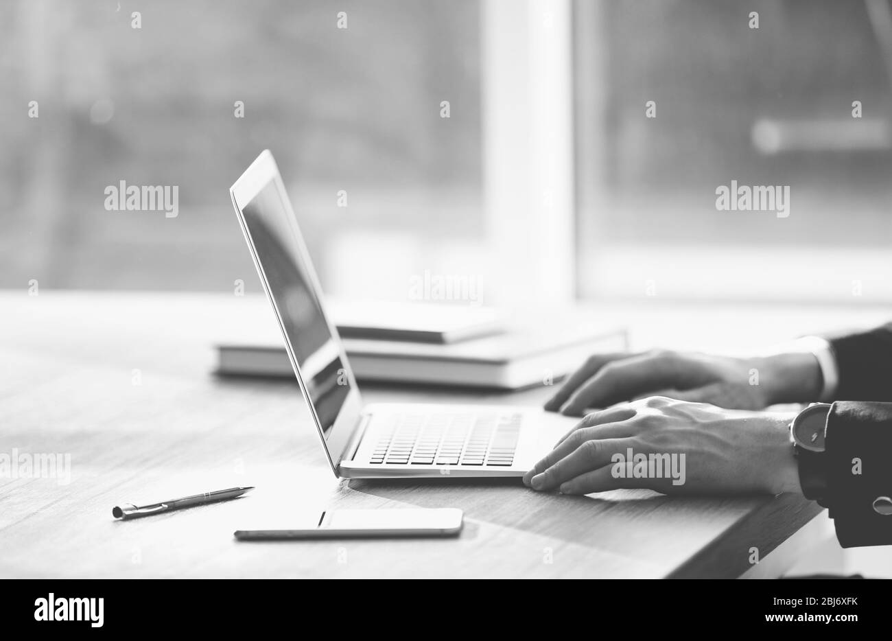 Les mains de l'homme utilisant un ordinateur portable à la table au bureau contre la fenêtre Banque D'Images