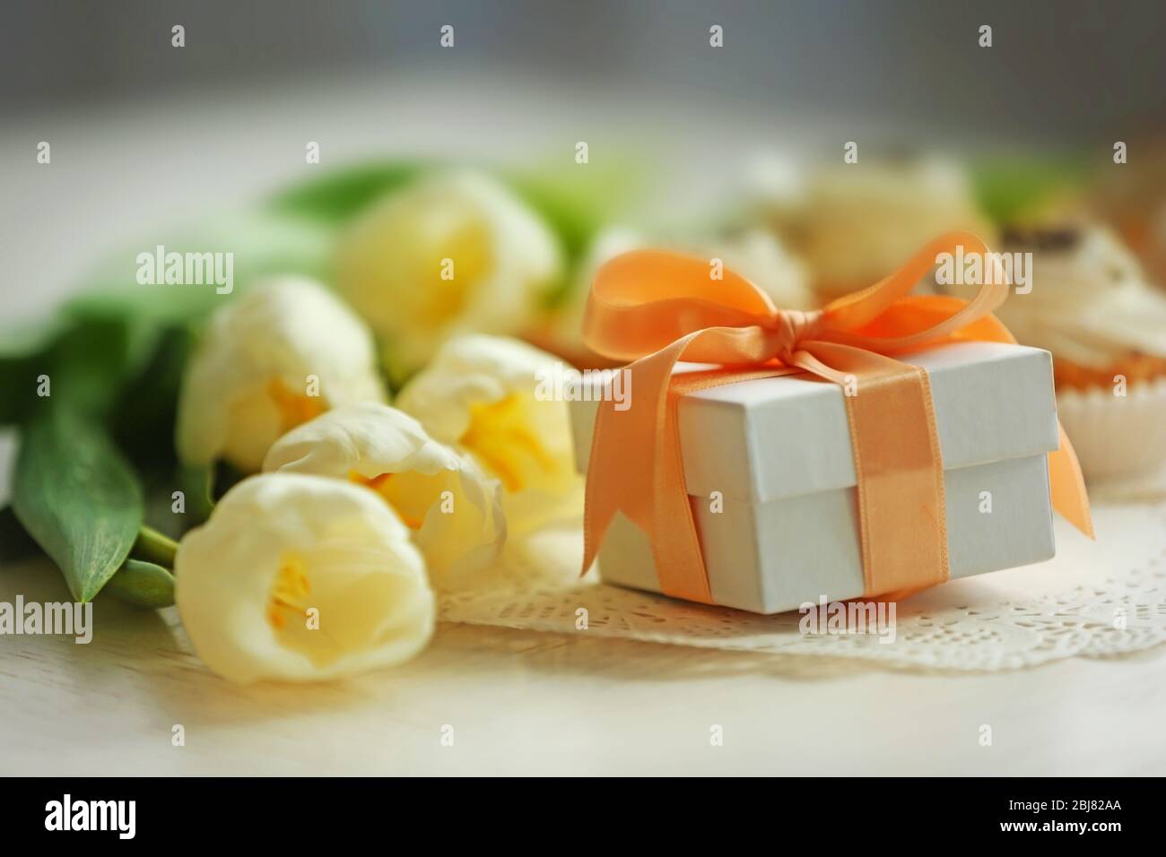 Un petit cadeau avec des tulipes de printemps blanches et de délicieux cupcakes sur une table blanche, gros plan Banque D'Images