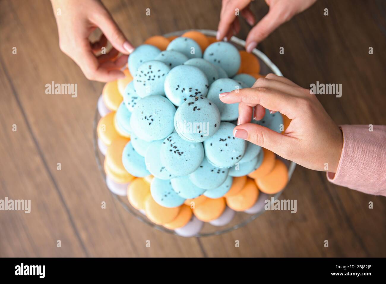 Mains féminines prenant de savoureux macarons de plat sur la table Banque D'Images