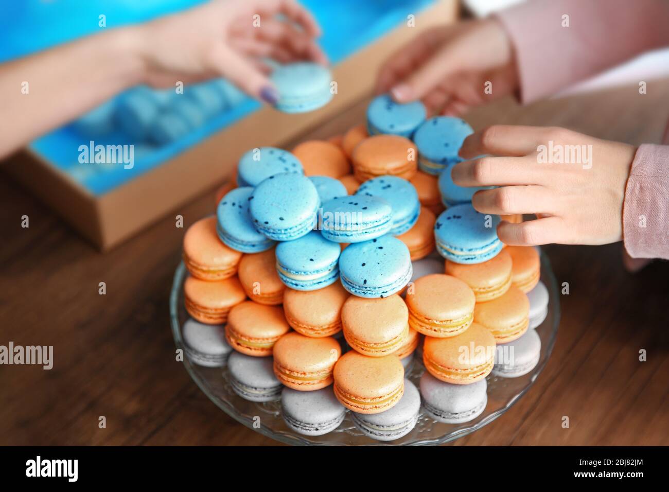 Mains féminines prenant de savoureux macarons de plat sur la table Banque D'Images