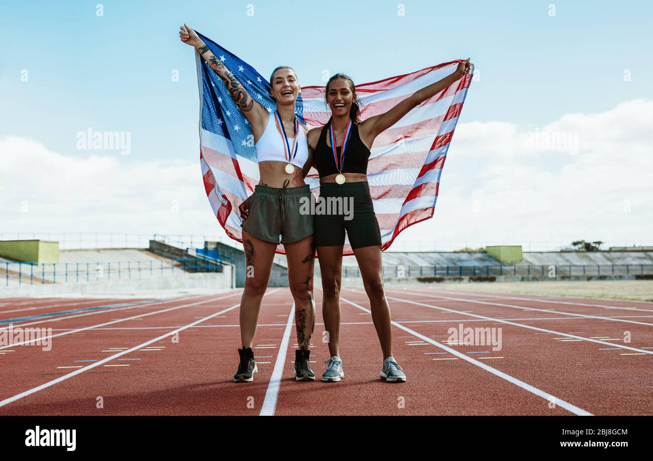 Deux coureurs de femmes qui célèbrent sur la bonne voie avec le drapeau américain. Athlète gagnant tenant le drapeau américain derrière au stade. Banque D'Images