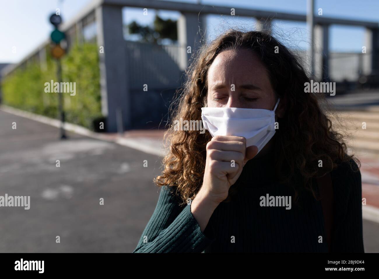 Femme caucasienne portant un masque de protection et toussant dans la rue Banque D'Images