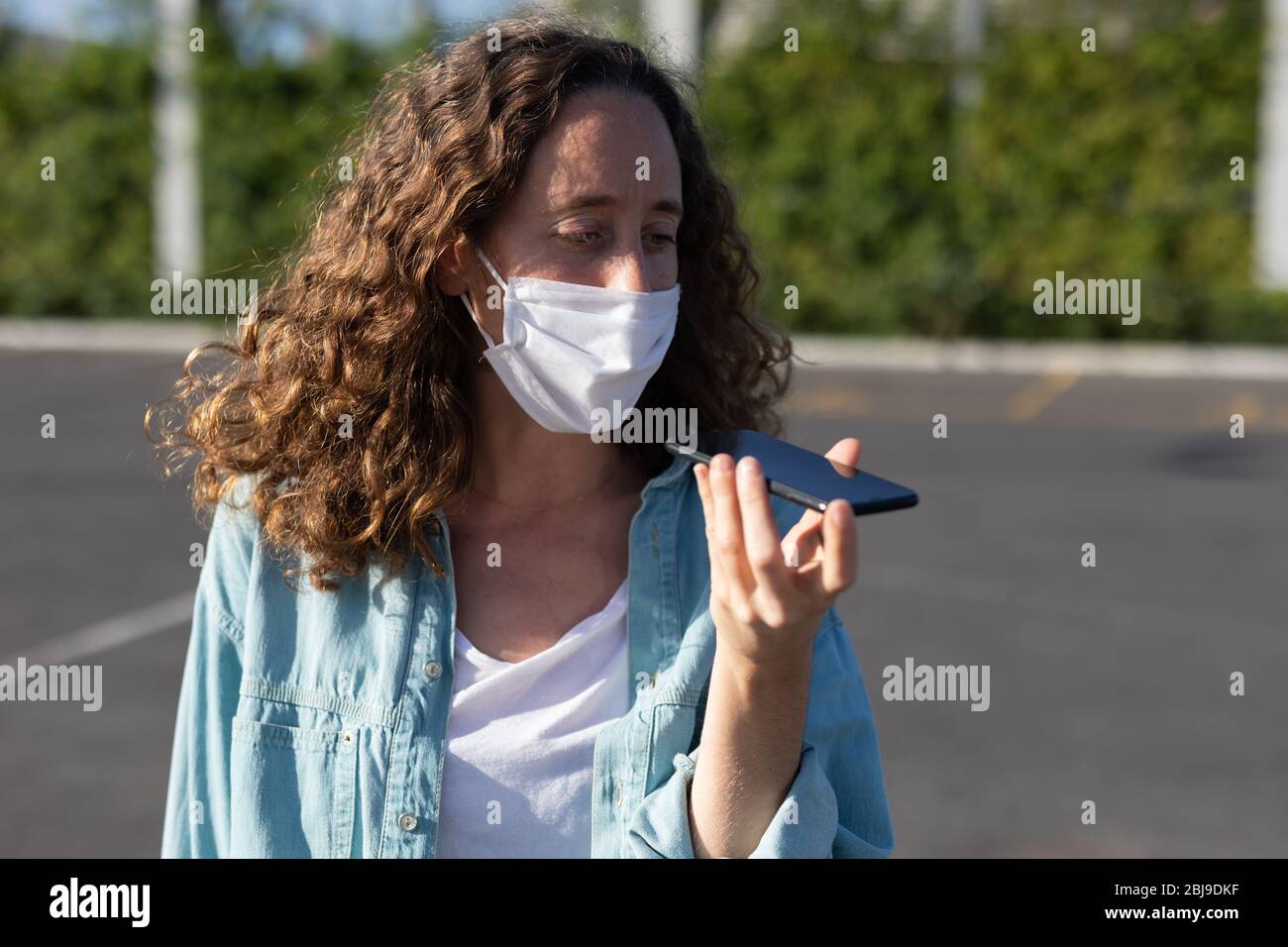 Femme caucasienne portant un masque de protection dans la rue et utilisant son téléphone Banque D'Images