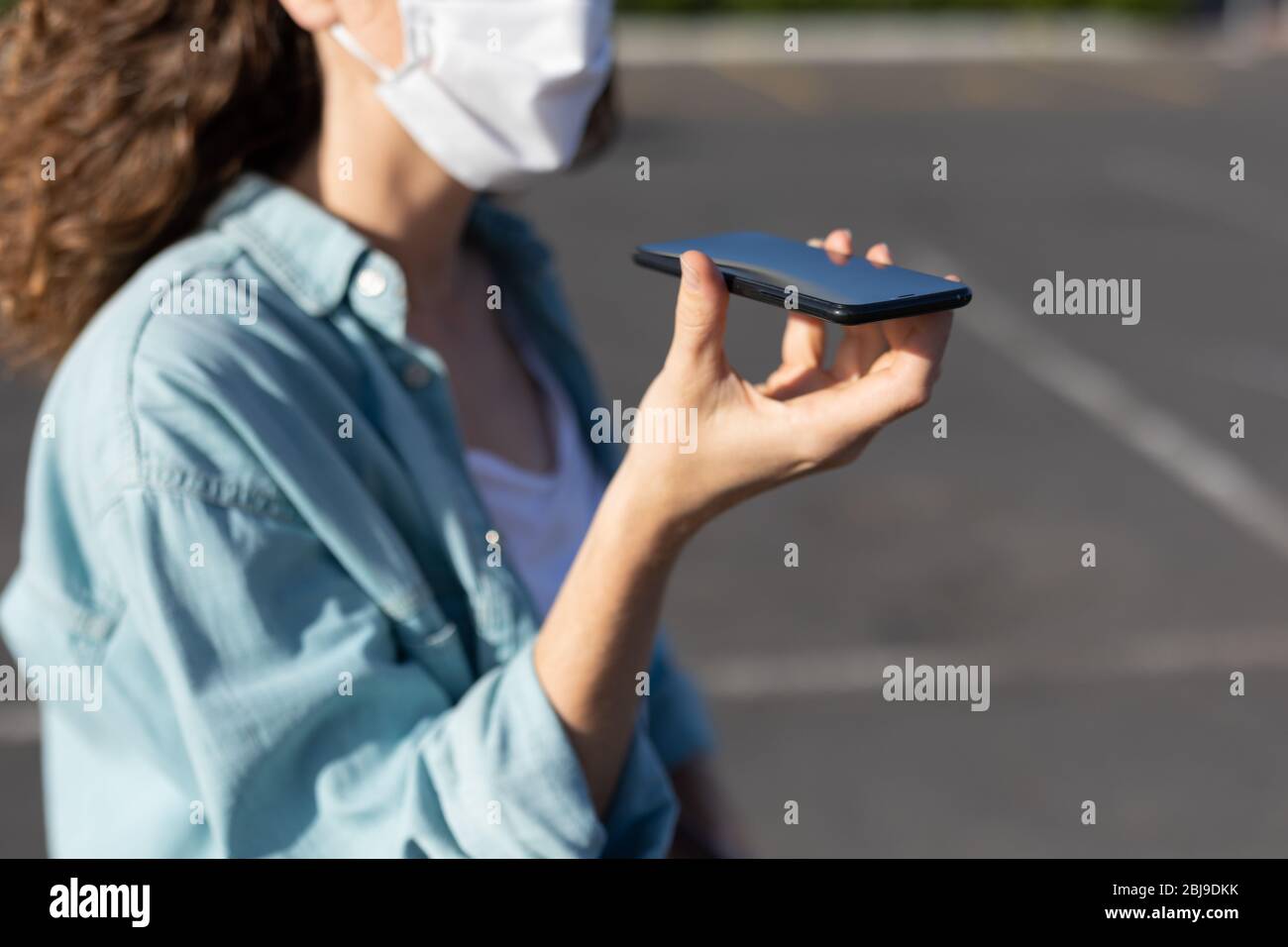 Femme caucasienne portant un masque de protection dans la rue et utilisant son téléphone Banque D'Images