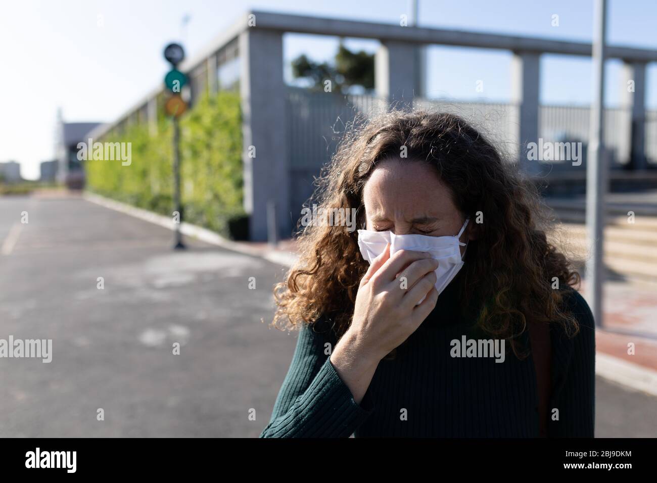 Femme caucasienne portant un masque de protection et toussant dans la rue Banque D'Images