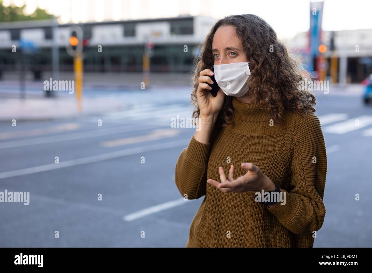 Femme caucasienne portant un masque de protection et utilisant son téléphone dans la rue Banque D'Images