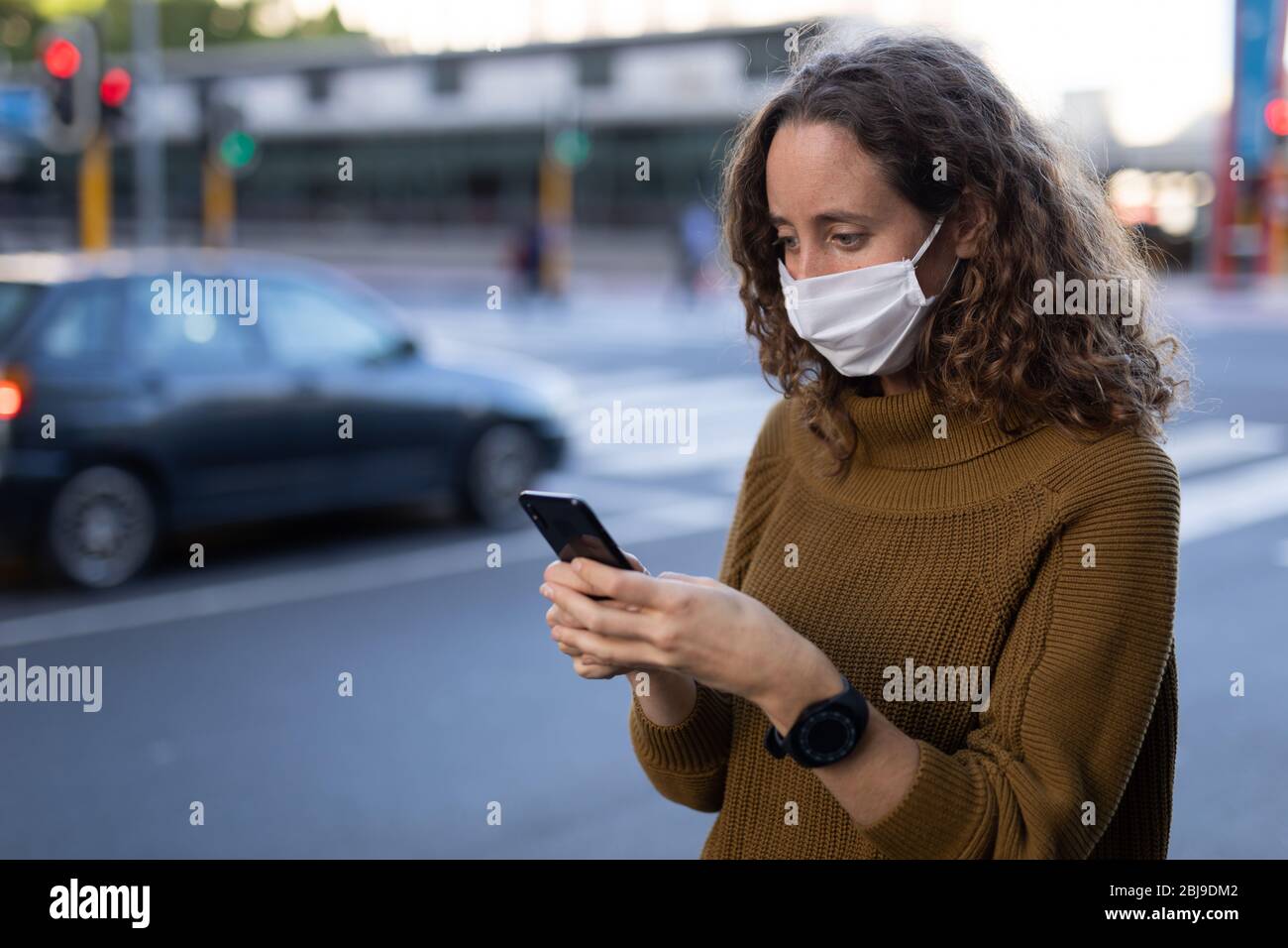 Femme caucasienne portant un masque de protection et utilisant son téléphone dans la rue Banque D'Images