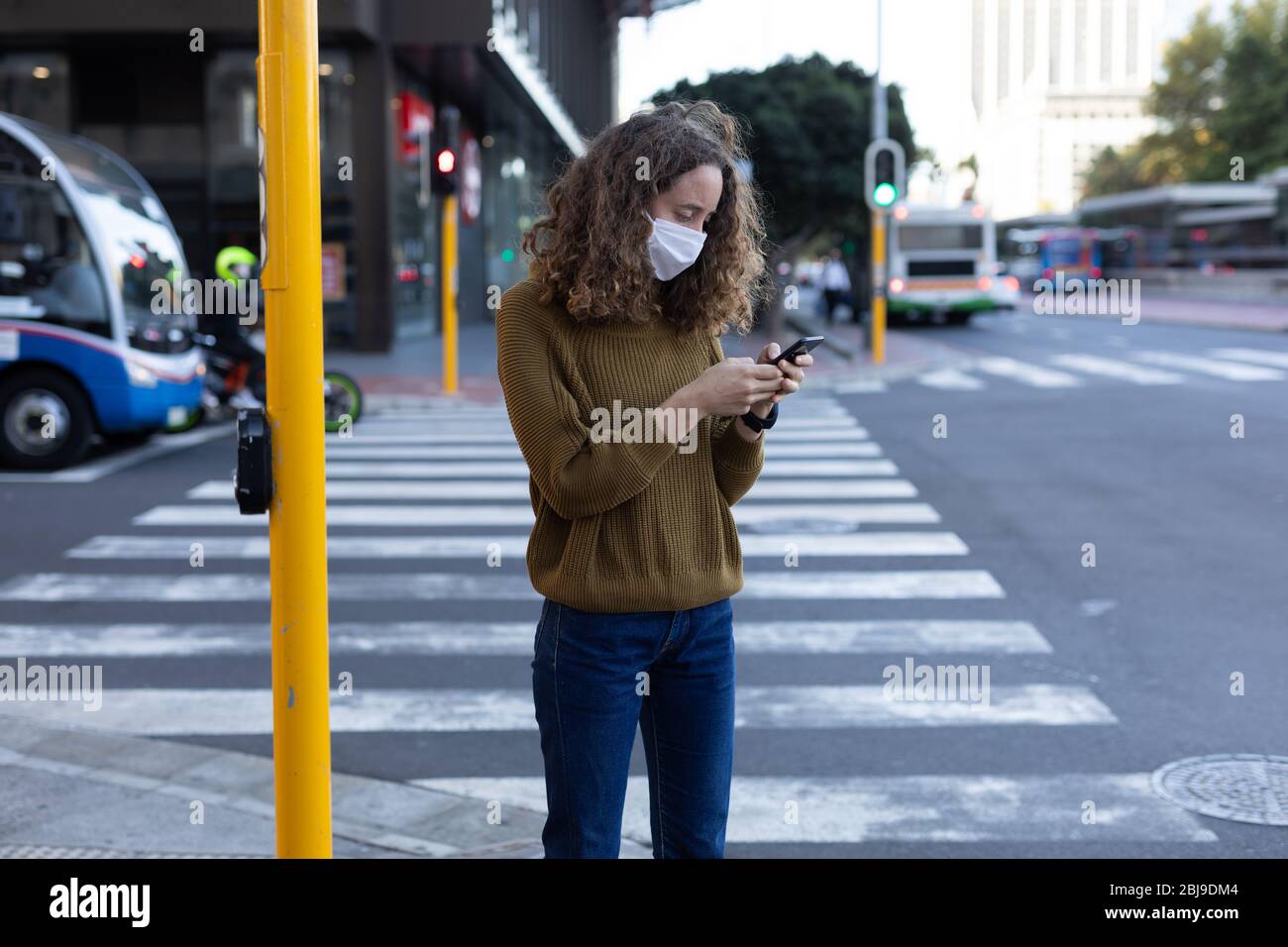 Femme caucasienne portant un masque de protection et utilisant son téléphone dans la rue Banque D'Images